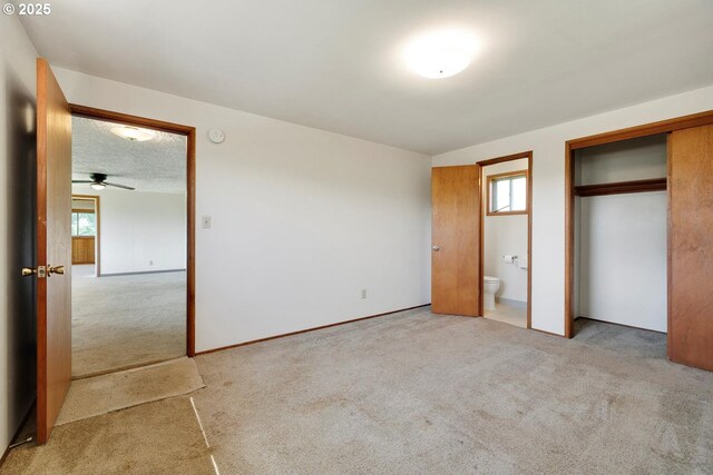 unfurnished bedroom with a closet, carpet, ensuite bathroom, and multiple windows