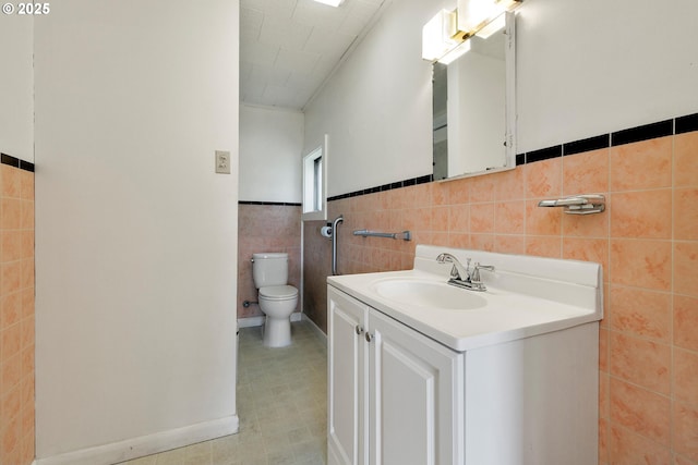 bathroom featuring wainscoting, vanity, toilet, tile patterned floors, and tile walls
