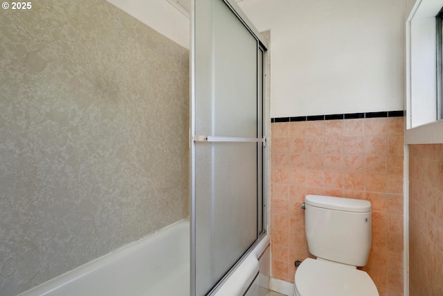 bathroom with enclosed tub / shower combo, toilet, tile walls, and a wainscoted wall