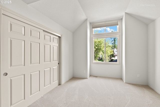unfurnished bedroom with lofted ceiling, light colored carpet, a textured ceiling, a closet, and baseboards
