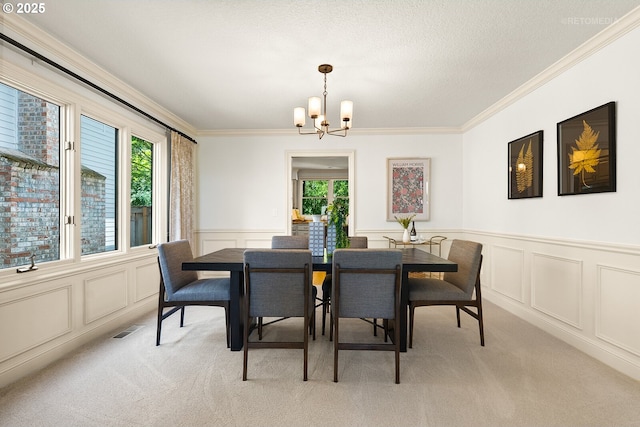 dining space featuring a decorative wall, light carpet, a chandelier, ornamental molding, and wainscoting