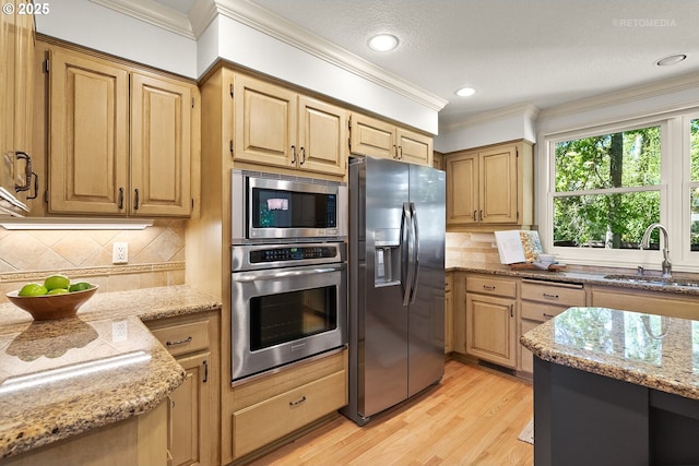 kitchen with appliances with stainless steel finishes, a sink, light stone counters, crown molding, and light wood finished floors