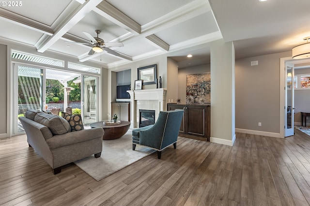 living area with wood-type flooring, a ceiling fan, baseboards, and a glass covered fireplace