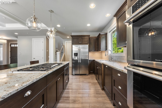 kitchen with decorative backsplash, dark brown cabinetry, a sink, light wood-style floors, and built in appliances