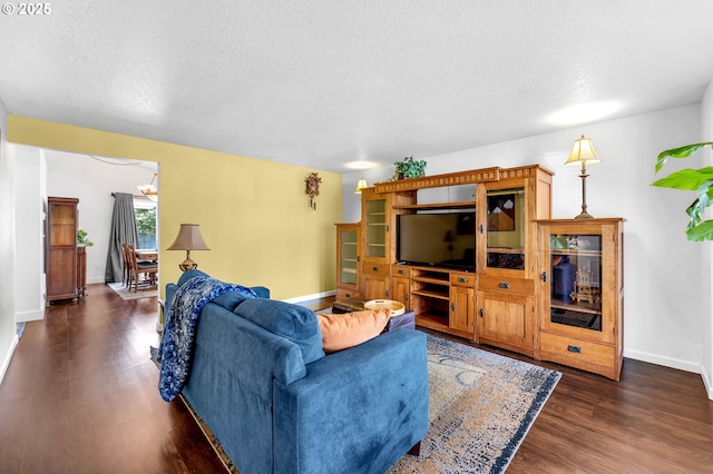 living room featuring a textured ceiling, dark wood-style flooring, and baseboards