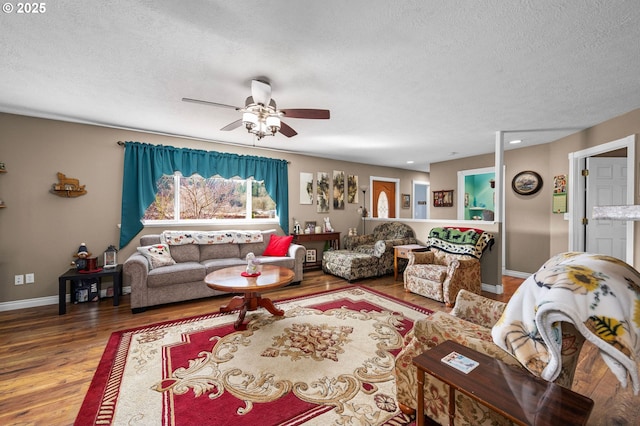 living room with a ceiling fan, a textured ceiling, baseboards, and wood finished floors