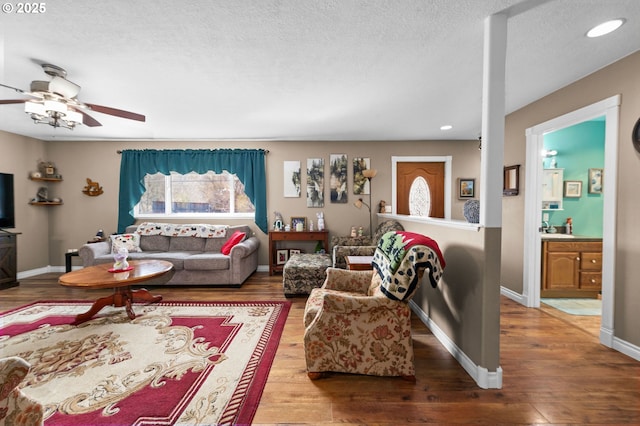 living room featuring a textured ceiling, ceiling fan, recessed lighting, wood finished floors, and baseboards