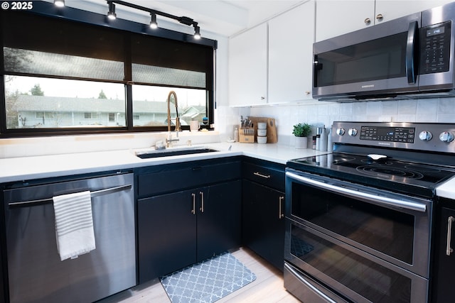 kitchen featuring light countertops, decorative backsplash, appliances with stainless steel finishes, white cabinetry, and a sink