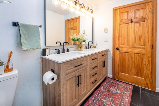 bathroom with double vanity, a sink, toilet, and an inviting chandelier