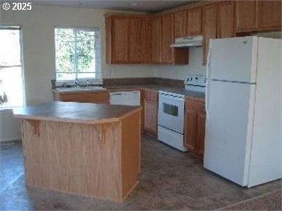 kitchen with under cabinet range hood, white appliances, a sink, and a center island