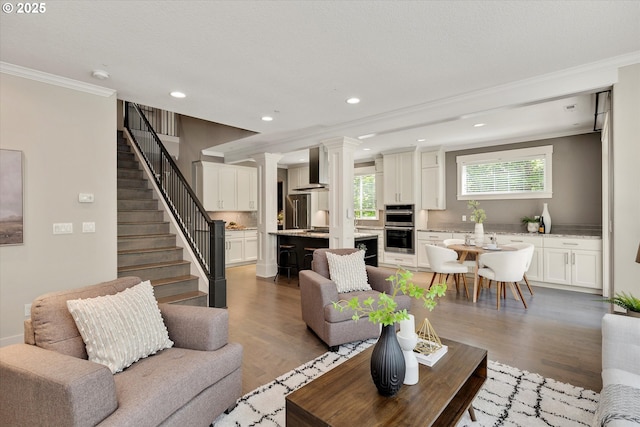 living area featuring decorative columns, dark wood finished floors, stairs, crown molding, and recessed lighting