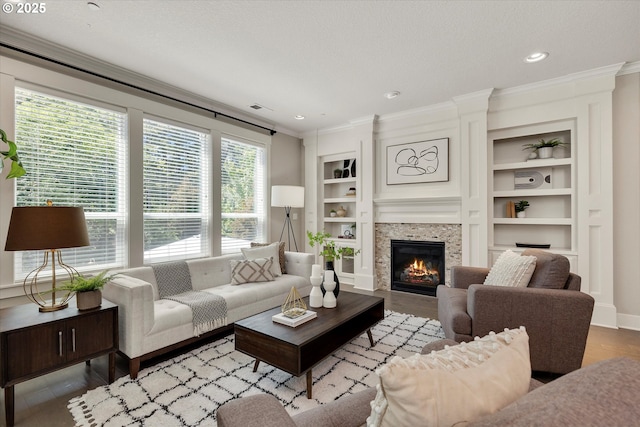 living room featuring built in features, crown molding, light wood finished floors, visible vents, and a tile fireplace