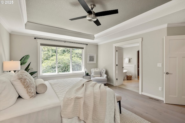 bedroom featuring light wood-style floors, visible vents, a tray ceiling, and ornamental molding