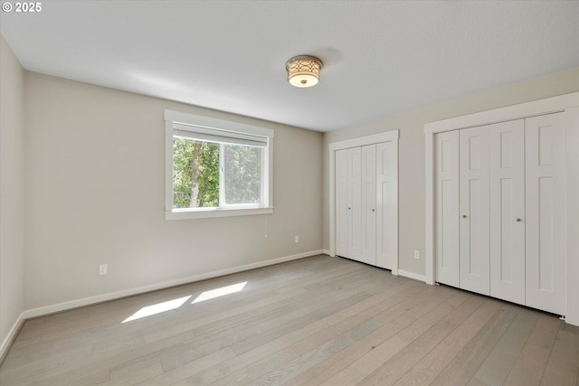 unfurnished bedroom featuring baseboards, light wood finished floors, and multiple closets