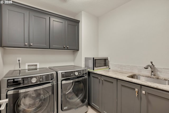 laundry room with cabinet space, a textured ceiling, a sink, and washing machine and clothes dryer