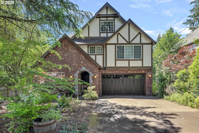 tudor house featuring a shingled roof, concrete driveway, stucco siding, an attached garage, and brick siding