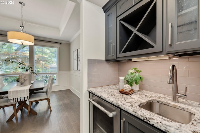 kitchen featuring gray cabinetry, a wainscoted wall, a sink, glass insert cabinets, and crown molding