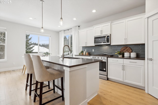 kitchen featuring hanging light fixtures, stainless steel appliances, sink, white cabinetry, and a kitchen island with sink