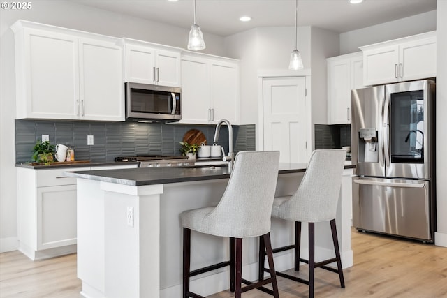 kitchen with white cabinetry, stainless steel appliances, decorative light fixtures, a kitchen island, and tasteful backsplash