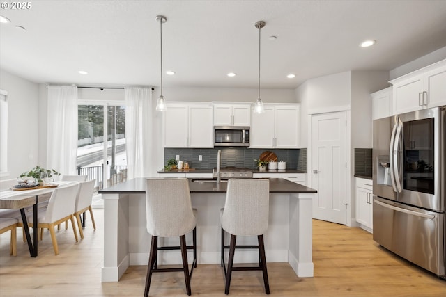 kitchen featuring an island with sink, white cabinetry, stainless steel appliances, and decorative light fixtures