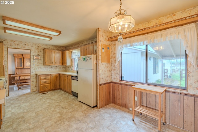 kitchen featuring wallpapered walls, light countertops, dishwashing machine, wainscoting, and freestanding refrigerator