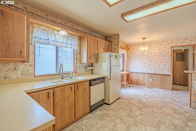 kitchen featuring a sink, wallpapered walls, white appliances, wainscoting, and light countertops