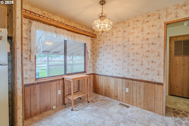 unfurnished dining area featuring visible vents, an inviting chandelier, wood walls, wainscoting, and wallpapered walls