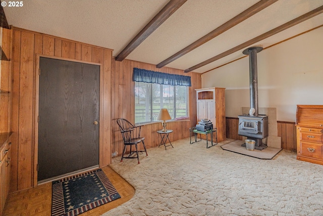 sitting room featuring a wood stove, vaulted ceiling with beams, wooden walls, and a textured ceiling