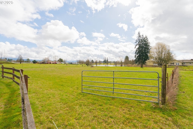 view of gate with a yard, a rural view, and fence