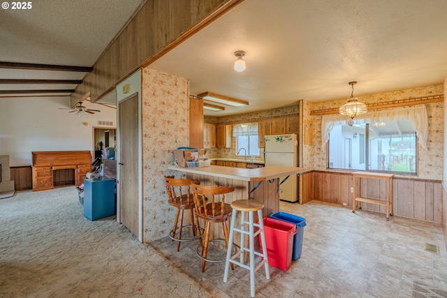 kitchen featuring a peninsula, freestanding refrigerator, a sink, light countertops, and brown cabinets