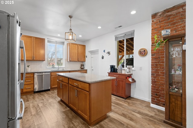 kitchen with light wood-style flooring, appliances with stainless steel finishes, a kitchen island, a sink, and light stone countertops