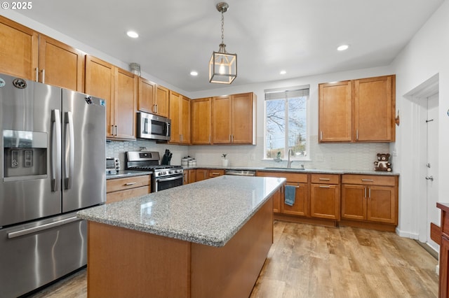 kitchen with decorative light fixtures, light wood-style flooring, appliances with stainless steel finishes, a sink, and light stone countertops