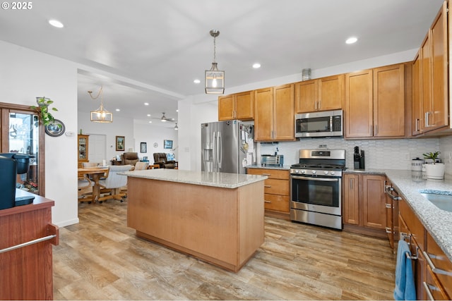 kitchen featuring light stone counters, stainless steel appliances, light wood-style floors, a center island, and tasteful backsplash