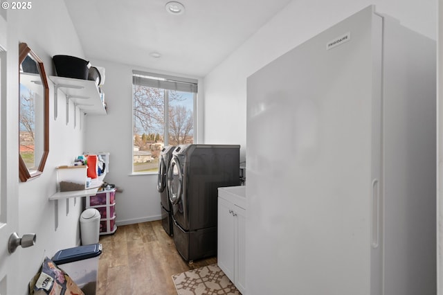 laundry room with light wood-type flooring, cabinet space, baseboards, and washer and clothes dryer