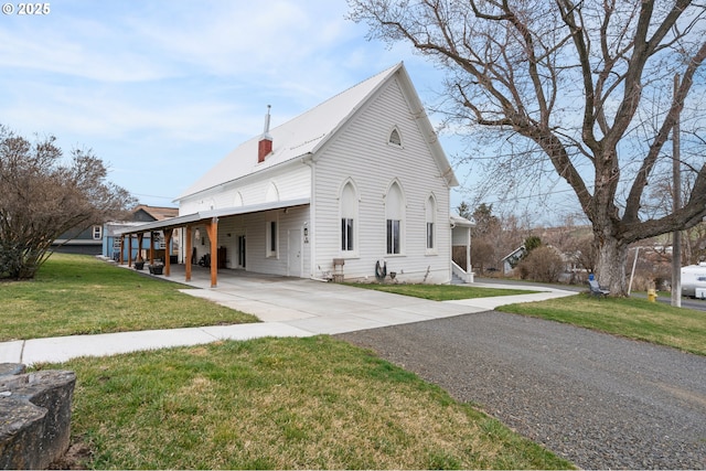 view of side of property with an attached carport, concrete driveway, a lawn, and a chimney