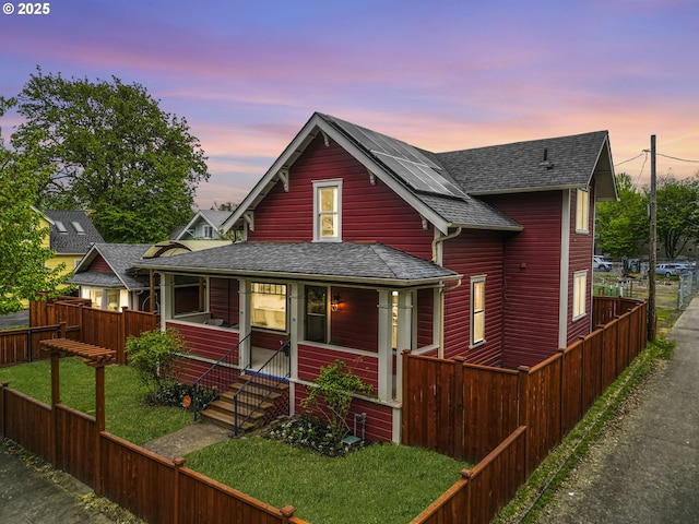 view of front of home featuring a fenced backyard, a front lawn, roof with shingles, and solar panels