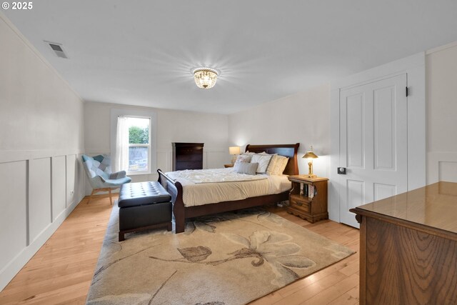 bedroom featuring a decorative wall, light wood finished floors, and visible vents
