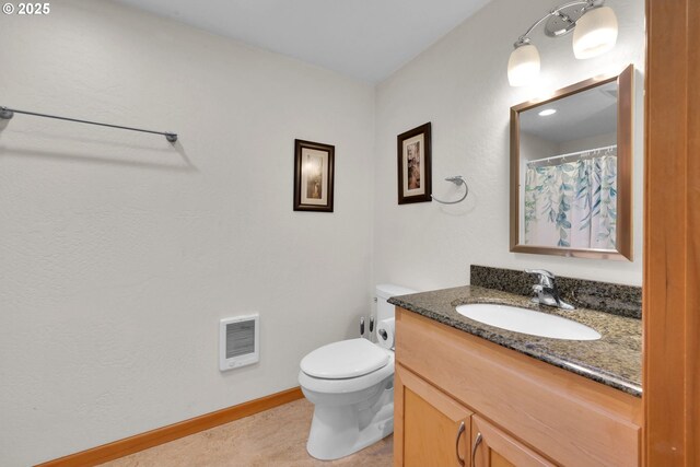 bathroom with heating unit, vanity, baseboards, and toilet