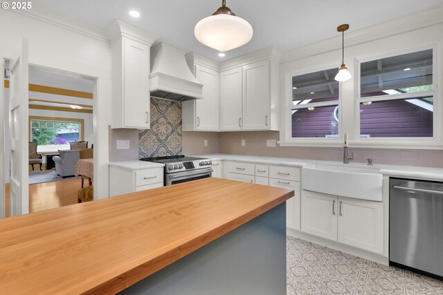 kitchen with hanging light fixtures, a sink, butcher block countertops, premium range hood, and stainless steel appliances