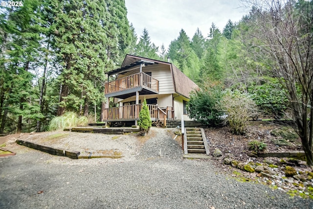 view of front of house featuring a forest view, a wooden deck, stairway, and roof with shingles