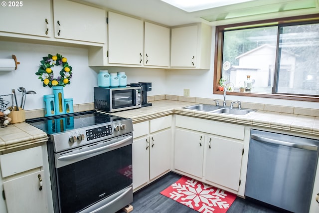 kitchen with dark wood finished floors, tile countertops, appliances with stainless steel finishes, white cabinetry, and a sink