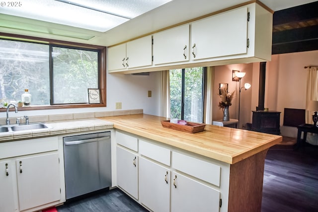 kitchen featuring dark wood-type flooring, a wood stove, a sink, dishwasher, and a peninsula