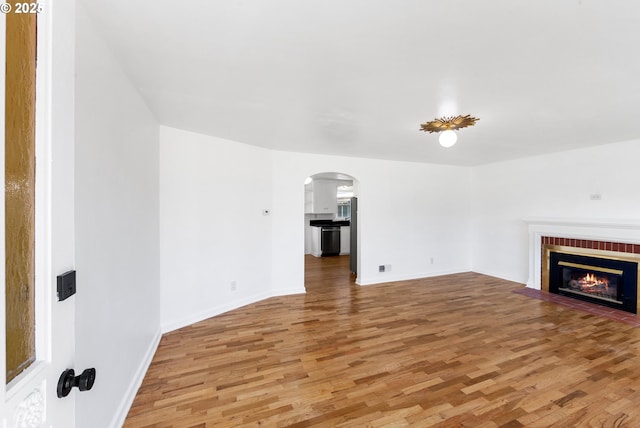 unfurnished living room with hardwood / wood-style flooring and a brick fireplace