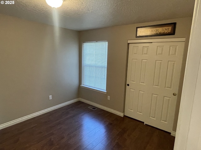 unfurnished bedroom with a closet, a textured ceiling, baseboards, visible vents, and dark wood-style floors