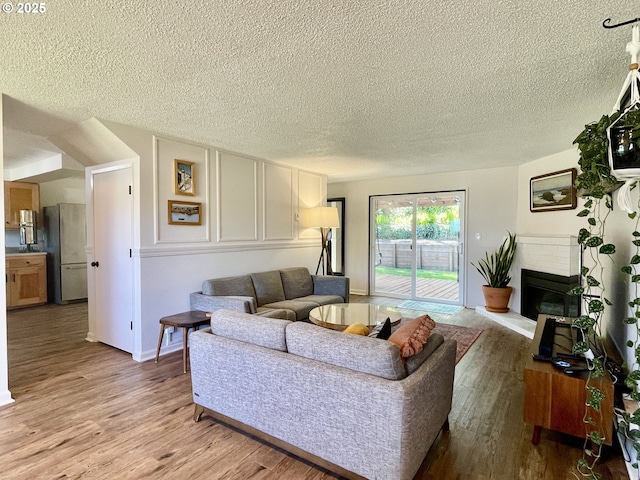 3851 Edgewood Dr, North Bend, OR 97459 - living room featuring a textured ceiling, light wood-type flooring, a fireplace with raised hearth, and baseboards