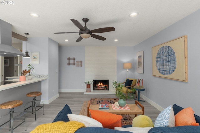living room featuring a fireplace, light wood-style floors, baseboards, recessed lighting, and a ceiling fan