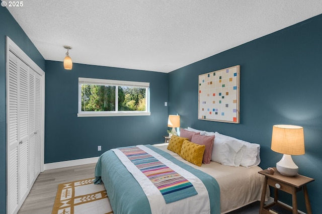 bedroom with a textured ceiling, baseboards, wood finished floors, and a closet