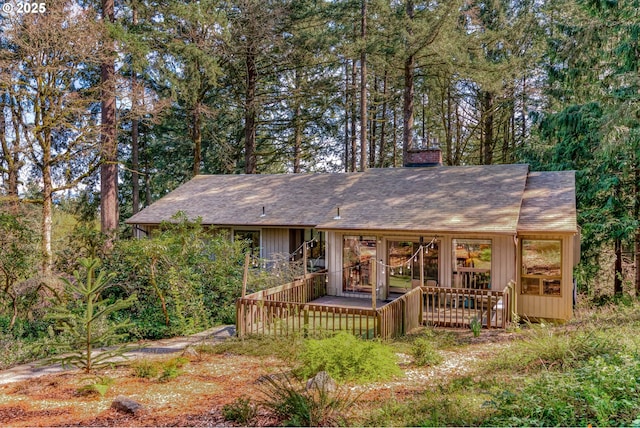 rear view of house featuring roof with shingles, a wooden deck, and a chimney
