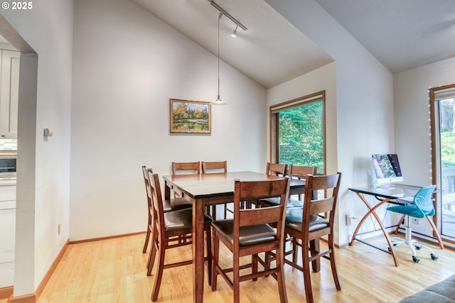 dining space featuring baseboards, track lighting, lofted ceiling, and light wood-type flooring