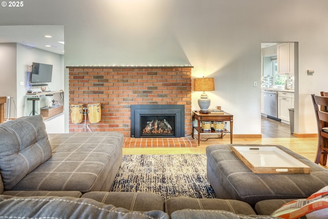 living room with a brick fireplace, recessed lighting, and wood finished floors